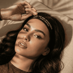 Woman wearing a headband with text, lying on a beige surface.