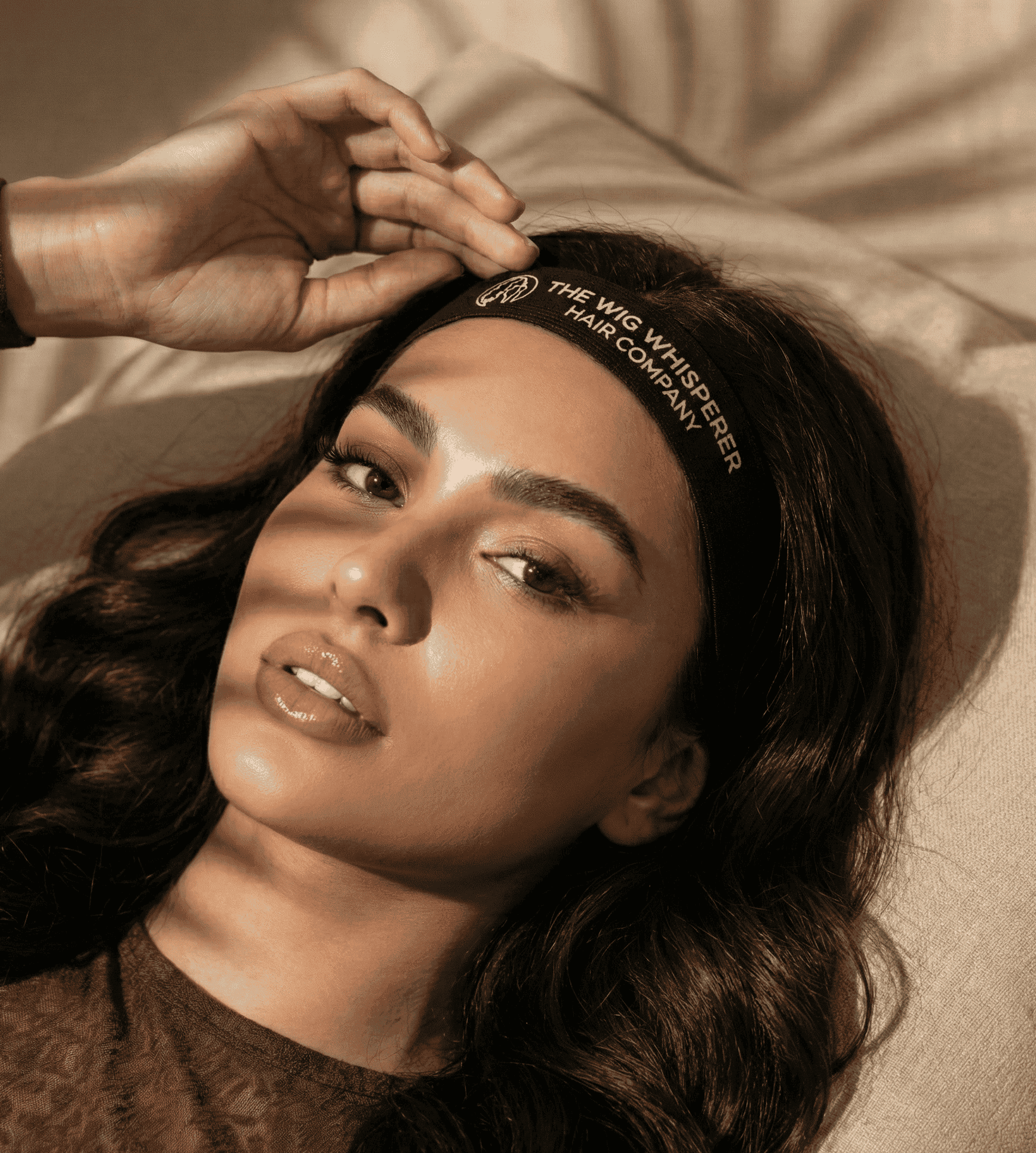 Woman wearing a headband with text, lying on a beige surface.