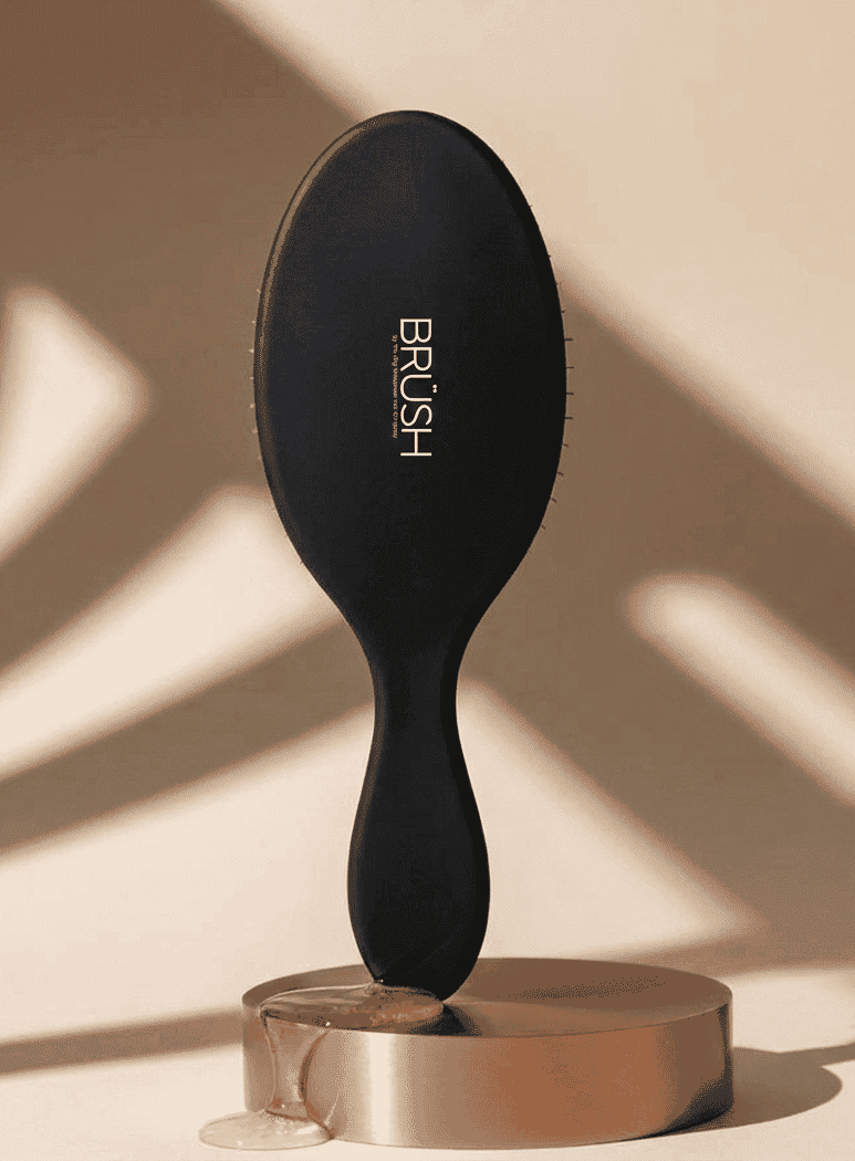 Black hairbrush on a bronze stand against a beige background